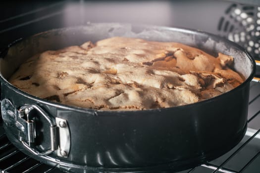 Baking dish with apple pie stands in black oven. Homemade seasonal bakery. Cooking in process