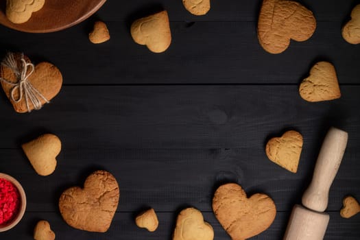 Gingerbread cookies and baking supplies on black wood background, copy space