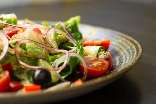 Vegetable salad with greens and olives in dark clay plate on wooden table