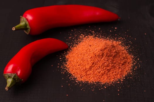 Two pods of red hot jalapeno peppers with a slide of pepper powder on a black wooden surface.