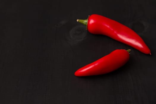 Two pods of red hot jalapeno peppers on a black wooden surface, copy space