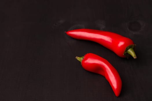 Two pods of red hot jalapeno peppers on a black wooden surface, copy space