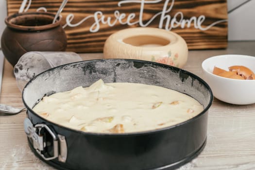 Baking dish with raw apple pie dough stands on kitchen counter next to ingredients, cooking utencils and wooden sign Home sweet home