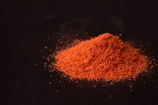 A pile of red hot pepper powder on a black wooden surface, copy space