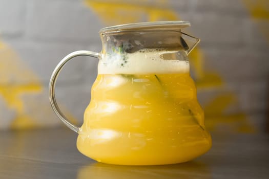 Yellow ginger tea with lemon and rosemary branch in transparent teapot on a wooden table