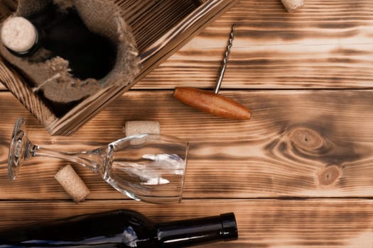 Wine glass, corkscrew, corks, wine bottles, grapevine on rustic burnt wooden background. Top view, copy space