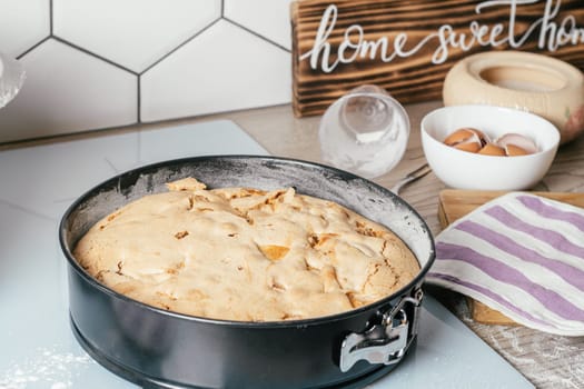 Baking dish with baked apple pie stands on kitchen counter next to ingredients, cooking utencils and wooden sign Home sweet home