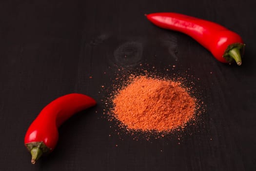 Two pods of red hot jalapeno peppers and a slide of pepper powder on a black wooden surface, copy space