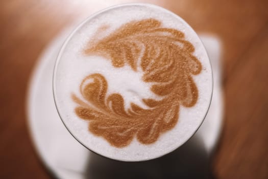 Delicious cappuccino coffee in cup mug glass latte with sour cream milk foam with pattern spike spica on white ceramic plate. Blurred brown table background. Lactose-free. Close up. Top view