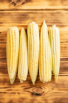 Five yellow milk sweet corn cobs ears maize with white granule green fresh ingredient product. Lie on wooden background table. Side cooking preparing dish. Top view. Close up choice flavor fillings.