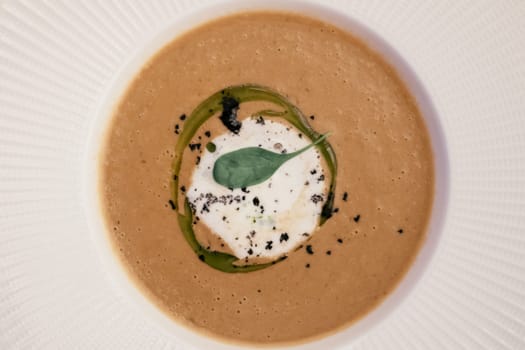 Tasty delicious thick brown pumpkin mushroom cream soup with mascarpone truffle pasta, herb sauce, green leaf in white circle mousse, condiment and seeds. White stripe plate background. Top view