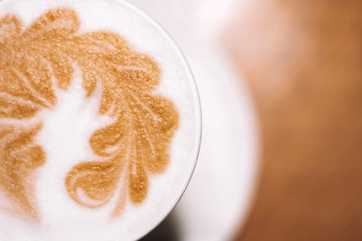 Delicious cappuccino coffee in cup mug glass latte with sour cream milk foam with pattern spike spica on white ceramic plate. Blurred brown table background. Lactose-free. Close up. Top view