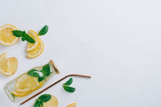 Glass bottle with lemonade with metal straw and ingredients for cooking. Ginger, lemon, mint on white surface. Flat lay, top view. Copy space