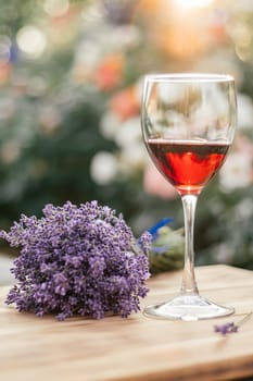 half-empty glass of red wine and lavender bouquet tied with blue ribbon on wooden brown table in sunny day at sunset in garden against organic background. soft focus. vertical