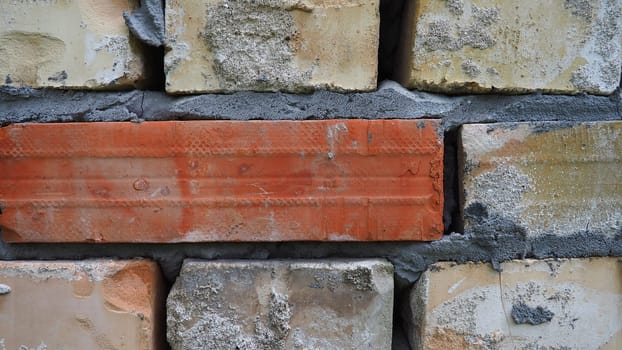 Brick wall. Ceramic masonry or fence. Old, uneven brick, covered in moss and mold in some places. The texture of the stone or mineral. The effect of moisture on brick structures. Village motifs