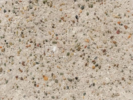 Concrete surface with multi-colored blotches of small stones. Light beige tone. Wall of a building or concrete slab. Close-up.