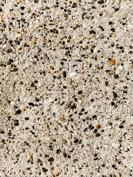 Concrete surface with multi-colored blotches of small stones. Light beige tone. Wall of a building or concrete slab. Close-up. Pockmarked cement surface. Interior or exterior finish option.