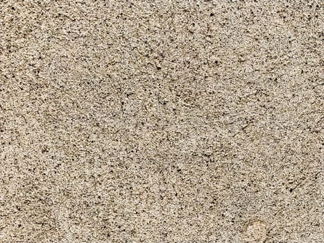 Concrete surface with multi-colored blotches of small stones. Light beige tone. Wall of a building or concrete slab. Close-up. Pockmarked cement surface. Interior or exterior finish option.