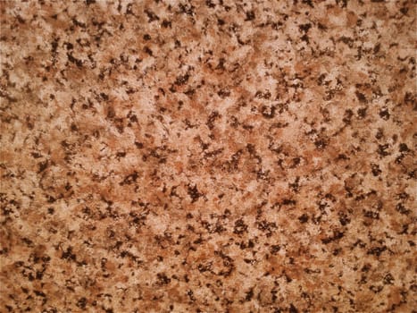 Granite smooth surface or slab in warm brown, gray, beige tones with frequent black spots and dots. Variant of interior decoration. Close-up. Natural background. Stone cut