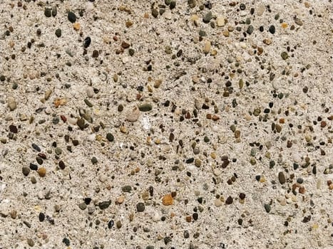 Concrete surface with multi-colored blotches of small stones. Light beige tone. Wall of a building or concrete slab. Close-up. Pockmarked cement surface. Interior or exterior finish option.