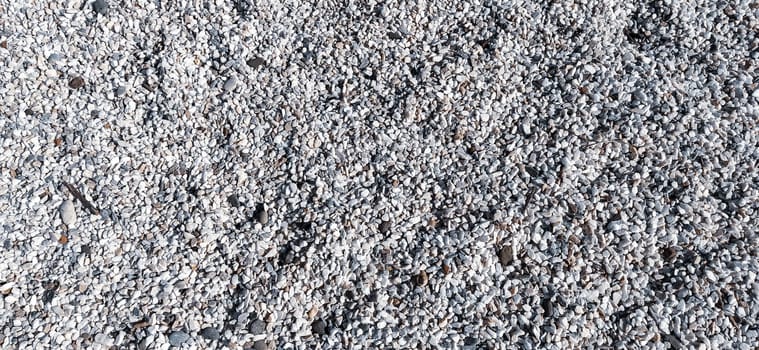 White small pebbles or decorative gravel. Natural daylight. The texture of the stone with a rough surface. Pebble beach.