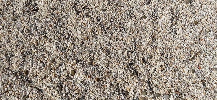 White small pebbles or decorative gravel. Natural daylight. The texture of the stone with a rough surface. Pebble beach.