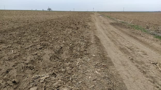 Plowed field. Arable land with fertile soil for planting crops. Rural landscape in Serbia, in the Balkans. Furrows and pits. On the right side is a dirt road. Panoramic view.