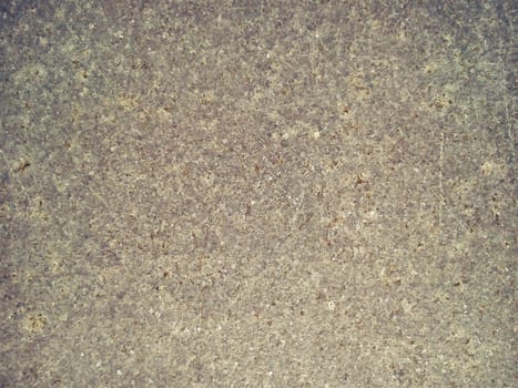 Granite is beige-brown in color with small light and dark specks, uneven scratches. The texture of the stone. Warm colors and shades. Dim background.
