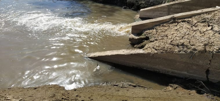 A large city drain drains sewage into a canal that flows into the river. Ecological problem. The concept of environmental protection and ecology. Concrete structure that removes contaminants into the water of the reservoir