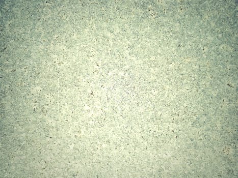 Granite of green-grey color with small light and dark specks, uneven scratches. The texture of the stone. Warm colors and shades. Dim background.