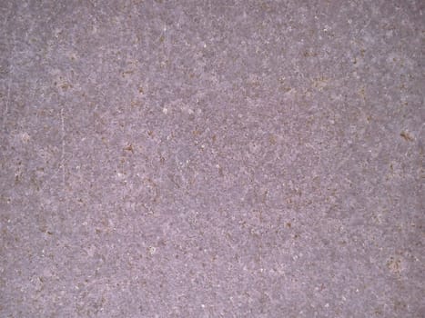 Granite of violet-pink color with small light and dark specks, uneven scratches. The texture of the stone. Warm colors and shades. Dim background.