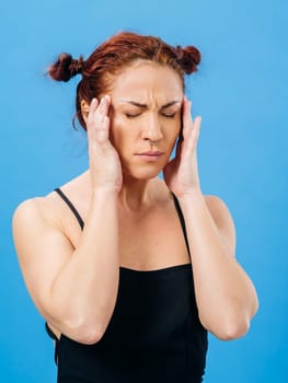 Beautiful redhead woman with headache or stress over blue background.