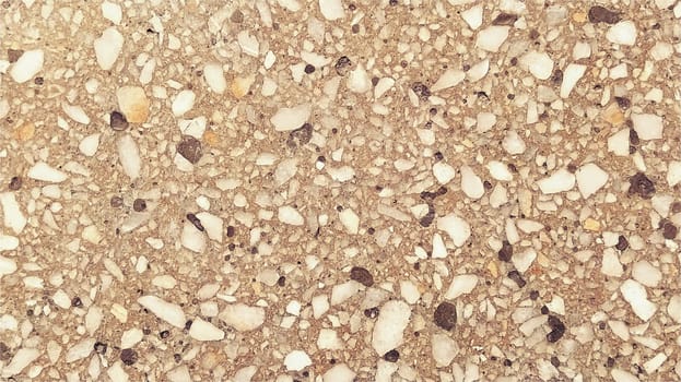Concrete surface with multi-colored spots of small stones. Beige or orange tone. Wall of a building or concrete slab. Close-up. Spotty cement surface. Interior or exterior decoration.