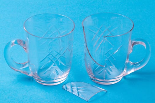 A whole and a broken wine glass with a shard of glass on a blue background. Macro.