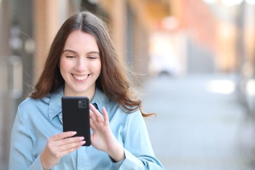 Front view portrait of a happy elegant woman checking smart phone in the street