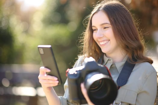 Happy photographer holding camera and checking phone in a park