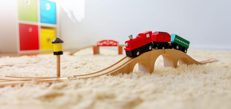 Closeup view of the toy train on the wooden bridge on the floor indoors. Panoramic background.