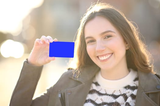 Happy woman showing credit card at camera in the street at sunset