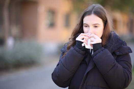 Ill woman using tissue to clean nose in the street in winter