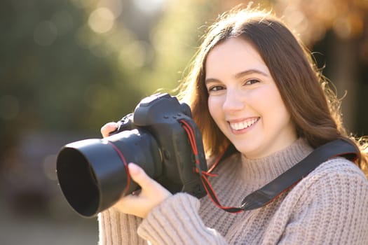 Happy photographer holding dslr camera looks at you in a park