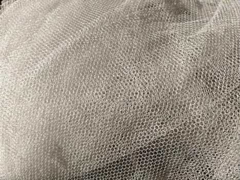 Sheer white net-like tulle. Mesh fabric wrinkled or folded carelessly. Close-up.