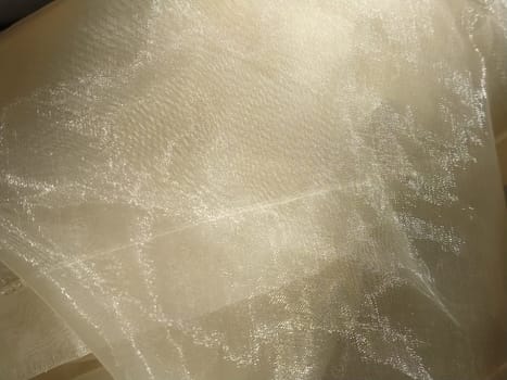 Organza in white and beige or champagne color close-up. Lightweight sheer tulle curtains under side lighting.