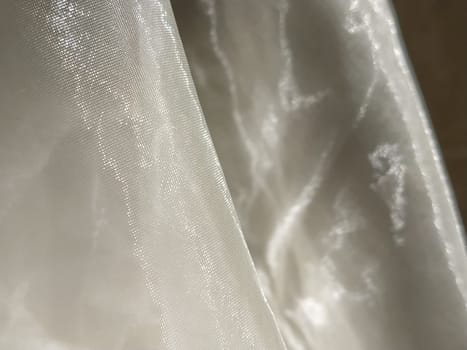 Organza in white and beige or champagne color close-up. Lightweight sheer tulle curtains under side lighting.