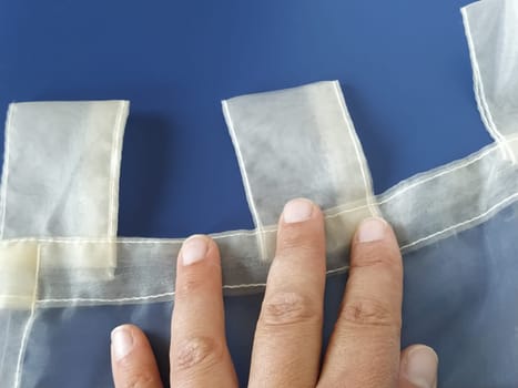 A seamstress's hand on a transparent organza. Loops on the tulle curtain. Sewing curtains. Blue background.