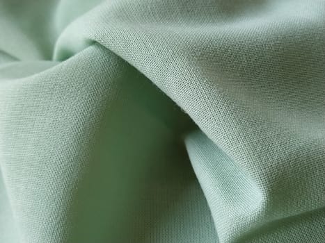 Close up of a woolen fabric of green color. Abstract canvas background, empty template. Thin natural fabric, wool or linen.