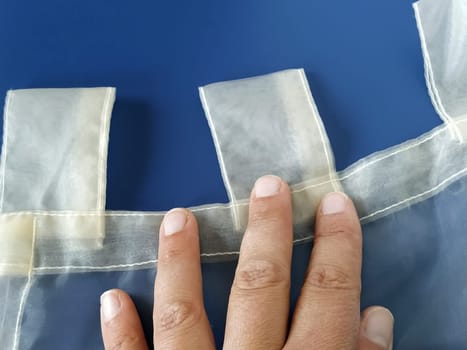 A seamstress's hand on a transparent organza. Loops on the tulle curtain. Sewing curtains. Blue background.