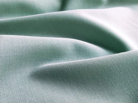 Beautifully folded light green fabric. Soft pleasant waves and flounces on textiles. Close-up. Drapery for curtains, fabric for dressmaking or upholstery.