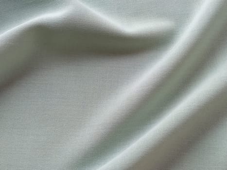 Beautifully folded light green fabric. Soft pleasant waves and flounces on textiles. Close-up. Drapery for curtains, fabric for dressmaking or upholstery.