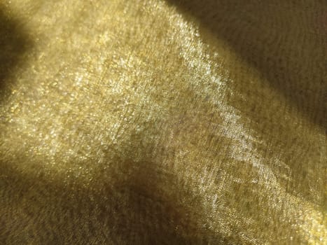 Beautiful gold fabric. Organza in yellow, orange, beige and brown shades. Pleats in the fabric. Shiny gradient under the light. Folded silky tulle. Transparent curtain material.