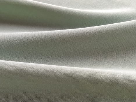 Beautifully folded light green fabric. Soft pleasant waves and flounces on textiles. Close-up. Drapery for curtains, fabric for dressmaking or upholstery.